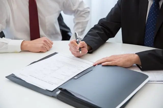 dos personas en un escritorio con un lapiz en la mano firmando un papel